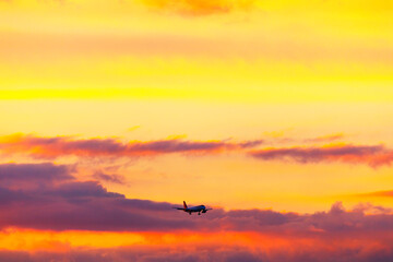 Plane is flying through a beautiful orange sky. Aircraft gliding gracefully across a bright sky, surrounded by fluffy colorful clouds