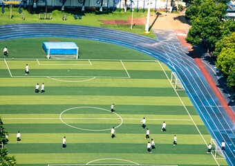 Aerial view of a group of students playing soccer on a school field with a surrounding track.