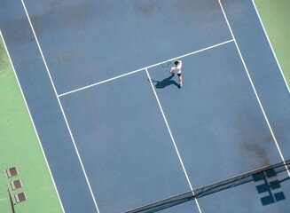 Aerial view of a tennis player practicing on a blue hard court