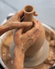Close-up of a potter's hands making a ceramic vase on a potter's wheel. Vertical photo. 