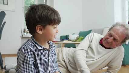 Fototapeta premium Young boy holding game cards, seated on floor with grandfather, engaged in indoor activity, family bonding time, intergenerational connection, cozy home setting, playful and educational