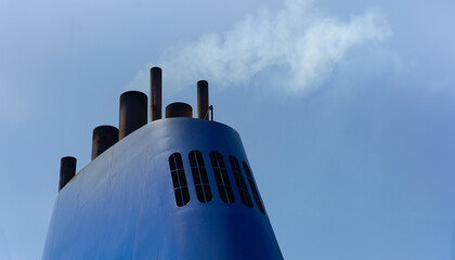 Blue chimney with dirty polluting plume of smoke on a ferry or cruise ship at blue sky
