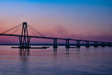 Puente Argentina, Chaco-Corrientes, en pleno atardecer, autos pasando, colores anaranjados, amarillos, rosa y morado
