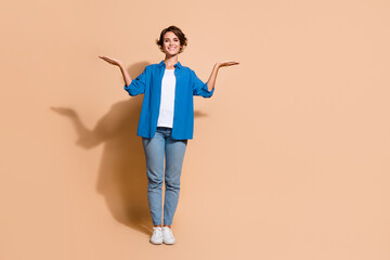Full body size photo cheerful young happy woman in blue shirt and jeans promoting two job offers isolated over beige color background
