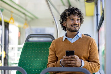 Smiling man sitting on bus seat using smartphone during commute. Relaxed expression capturing...