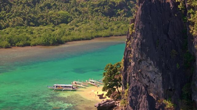 Aerial close up view of tropical paradise exotic island surrounded by crystal blue sea, sail boats and tourists. Travel video of Bukal island El Nido Philippines, untouched nature on sunny summer day