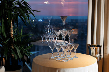 A Tower of Empty Glasses on a Table, Awaiting Bubbles, with Urban Skyline and Green Plant