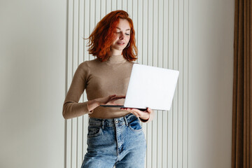 A Redheaded Girl with Curls Holding a Laptop, Highlighted by a Bright Wall