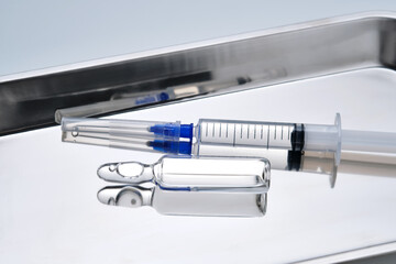 Syringes with needles and an ampoule in a stainless steel medical tray.
