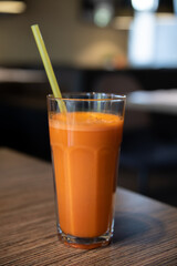 Close-up side view of fresh orange coloured carrot juice in drinking glass standing on wooden table in restaurant. Soft focus. Healthy eating theme.