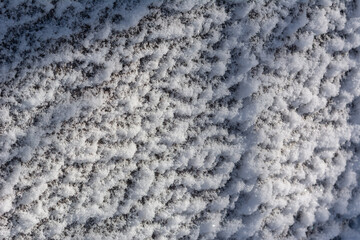 Texture of white fresh snow on ice or wall. Loose snowflakes close-up. Winter - December, January, February. White and blue colors. Play of light and shadow. Cold, sunny winter weather.