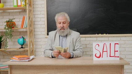Aged man college professor sit at desk in classroom in front of chalkboard with paper sign word sale on it and counting money. Education concept.