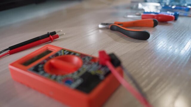 A close-up view of a workbench featuring various electronic tools, including a red multimeter, pliers, screwdrivers, and probes