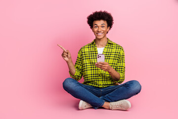Full length portrait of nice young man hold phone point finger empty space wear shirt isolated on pink color background