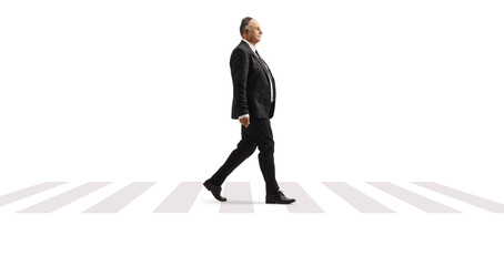 Full length profile shot of a mature businessman in a black suit walking at a pedestrian crossing