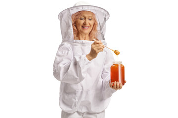 Apiarist in a uniform trying honey from a jar of honey and smiling