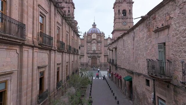 Morelia, Mexico. Soaring drone footage: Morelia's majestic cathedral, a UNESCO World Heritage Site, rises proudly with its pink stone fa&ccedil;ade, amidst vibrant city life and lively central square.