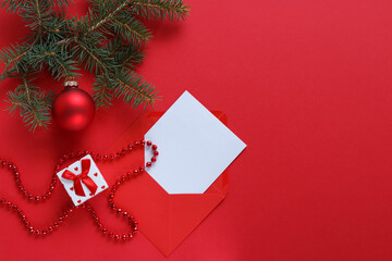 A pine branch on a red background with red Christmas decorations, a small gift box and a red envelope.
