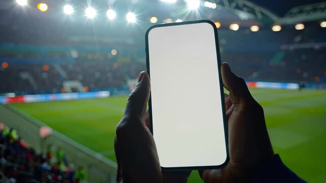 Close-up of a sport fan hand holding touching smartphone with blank white screen in a crowed football soccer stadium
