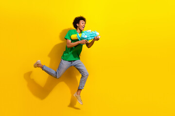 Full length photo of cheerful positive guy dressed green t-shirt jumping high shooting water gun emtpy space isolated yellow color background
