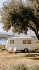 A white RV rests under a shade tree beside a tranquil blue sea on a warm summer day in Greece, creating a perfect getaway atmosphere