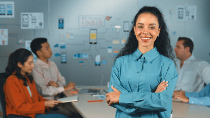 Hispanic professional businesswoman standing with arm folded at creative business meeting. Beautiful confident leader crossing arm while diverse business people discussion about plan. Manipulator.