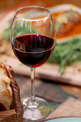 Glass of red wine, it shows a close-up of a glass of red wine sitting on a table, against a backdrop of greens and salad