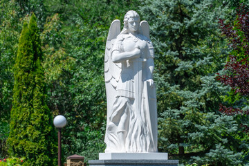 Angel statue holding sword and shield in christianity park. White sculpture exterminating angel...