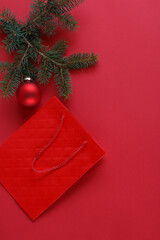 A red gift bag, a pine branch and Christmas decorations on a red background.