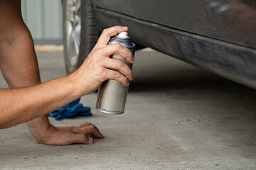 A man spray paints a car in a yard with black paint