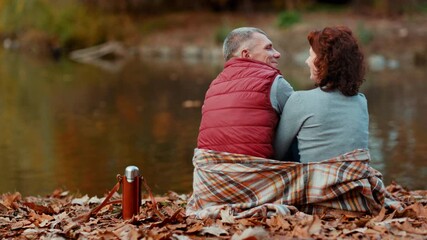 Hello autumn. Seen from behind modern couple in the park with blanket hugging.