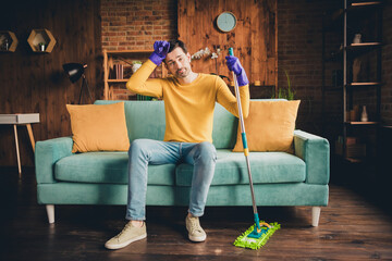 Obraz premium Full length photo of young guy mopping floor clean house sit couch tired dressed yellow garment spend pastime spacious house indoors room