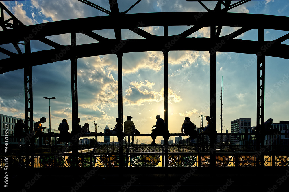 Wall mural silhouettes of young people sitting on the steel bridge in the sunset