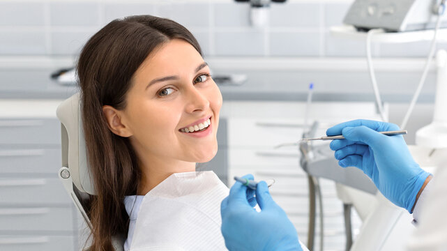 Young happy lady sitting in dentist chair, making regular check up in modern clinic, close up, free space