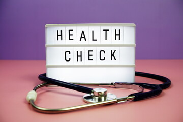Health Check letterboard text on LED Lightbox and stethoscope on pink and purple background