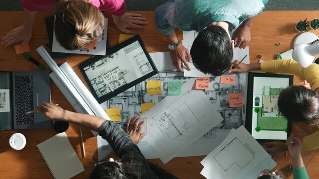 Top down view of manager writing project plan and sitting at meeting. Aerial view of business people planning and sharing idea about house construction at table with laptop and equipments. Symposium.