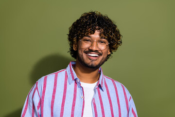 Fototapeta premium Portrait photo of smiling happy intelligent handsome arabian businessman in striped casual shirt and eyeglass isolated on khaki color background