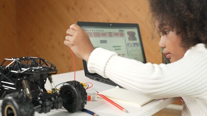 Smart african girl build robotic car while using wires while using laptop setting or writing prompt...