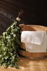 Sauna equipment. Bucket, birch whisk and towel on bamboo bench indoors