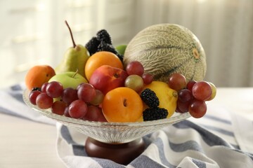 Glass vase with different fruits and berries on white table indoors, closeup