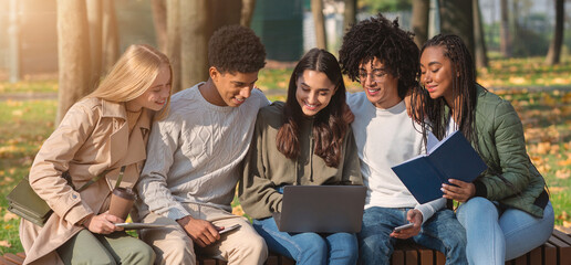Multiracial friends working on educational project while resting in public park, looking at laptop screen © Prostock-studio