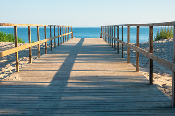 Perspective view of simple wooden path across sand dune. Sea and sky are visible. Background....