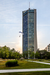 Fototapeta premium Prague, Czech Republic - July 19, 2024: A base jumper parachuting from atop a modern building in the outskirts of Prague 