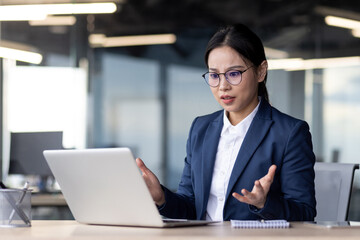 Asian businesswoman experiencing bad news on laptop, showing surprise and concern. Modern office...