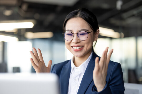 Happy asian businesswoman in office celebrating victory with laptop, showing excitement and success in online meeting.