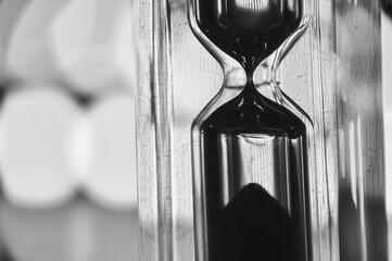 A black-and-white hourglass close-up measuring time with flowing sand transparent glass