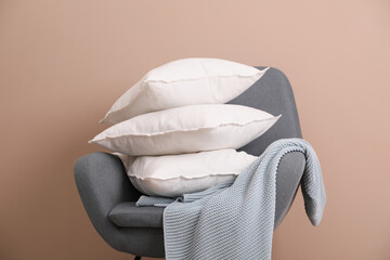 Stack of pillows, armchair and blanket near beige wall