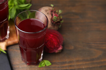 Fresh beet juice in glass and ripe vegetables on wooden table, closeup. Space for text