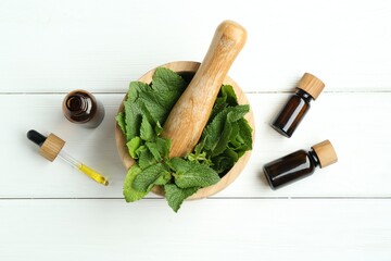 Tinctures in bottles, pipette, mortar, pestle and mint on white wooden table, flat lay