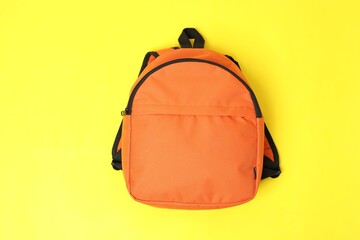 One orange backpack on yellow background, top view. Back to school